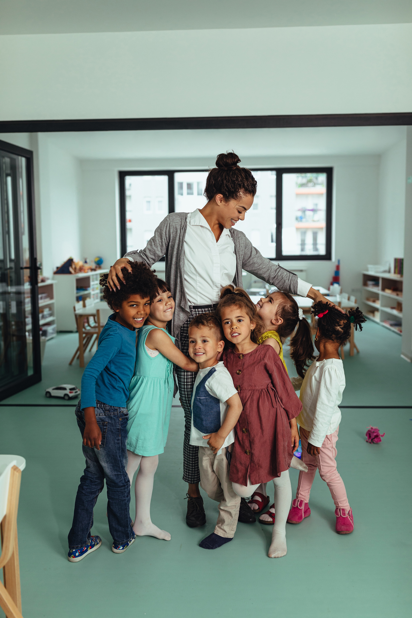 Teacher hugging diverse preschool children in classroom